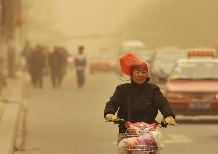 A woman wearing a plastic bag over her head rides along a street against wind on a hazy day in Taiyuan